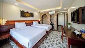 A hotel room with two beds, a TV, a desk, a brick fireplace, and a ceiling light. - Virgo Villa Que Hoi An (Hoi An)