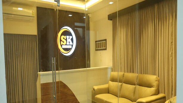 Un vestíbulo moderno con una pared de vidrio que muestra un logotipo, un sofá, un tapete estampado y un banco de madera.