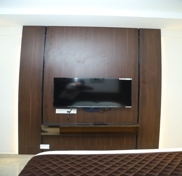 A flat-screen TV mounted on a wooden wall with a remote control on a stand below it. - SK Home Stay (Mayiladuthurai)