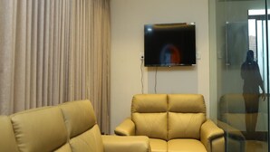 Una sala de estar moderna con un televisor de pantalla plana grande montado en la pared, un sofá de cuero color beige y una partición de vidrio.