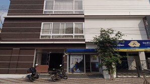 Un edificio de dos pisos con techo plano, una entrada visible y un cartel con texto.