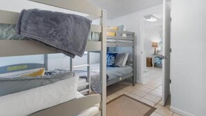 A dormitory room with bunk beds, a ceiling fan, and a visible door leading to another room. - Fenway Fiddler - Steinhatchee (Steinhatchee)