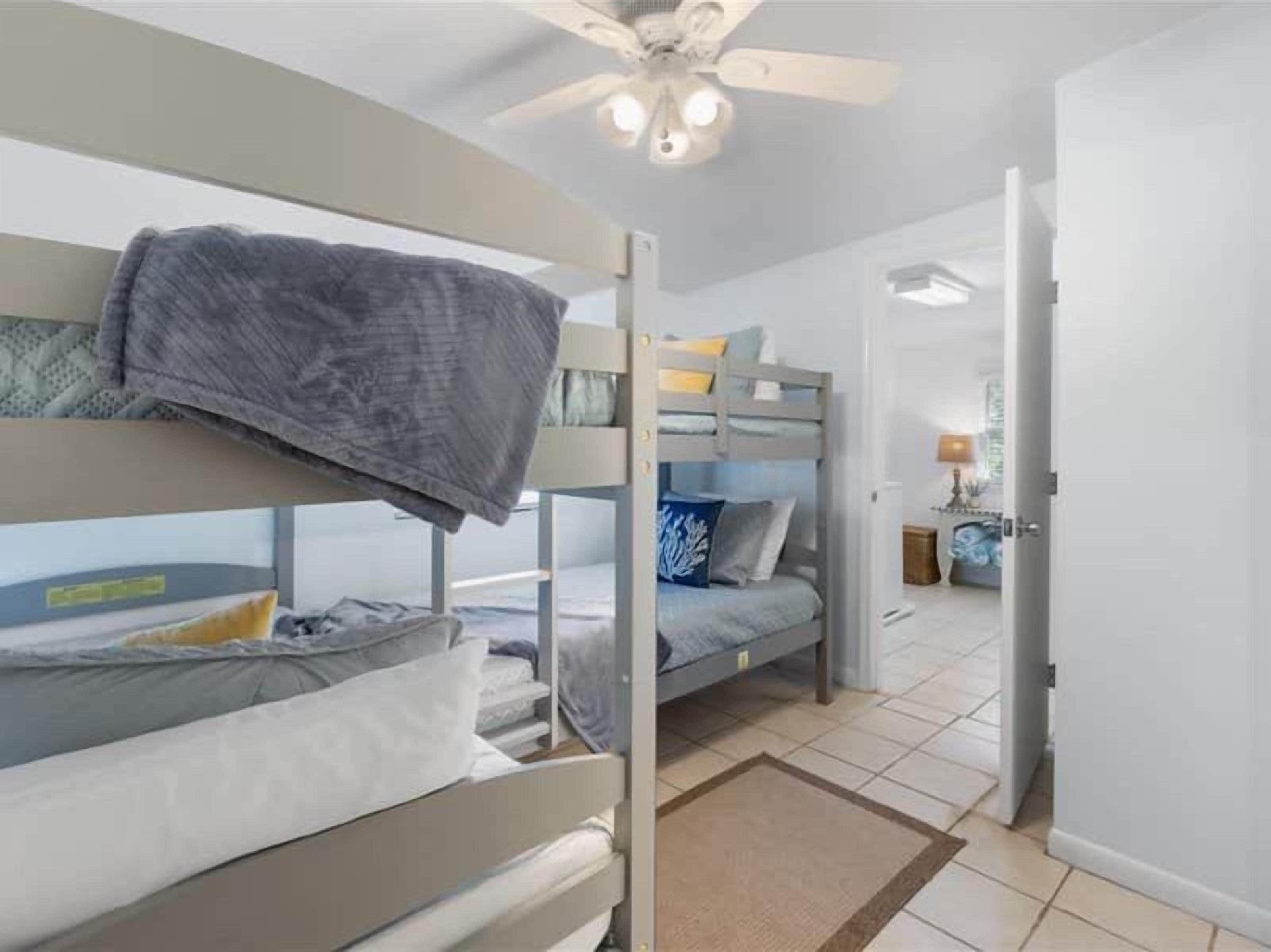 A dormitory room with bunk beds, a ceiling fan, and a visible door leading to another room.