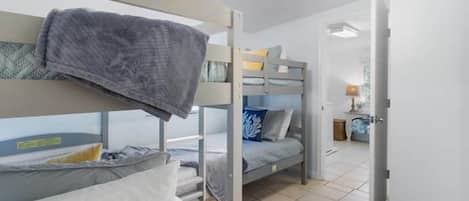 A dormitory room with bunk beds, a ceiling fan, and a visible door leading to another room.