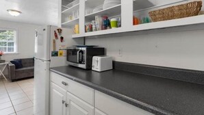A modern kitchen with white cabinets, a black countertop, a microwave, a toaster, and various kitchen utensils. - Fenway Fiddler - Steinhatchee (Steinhatchee)