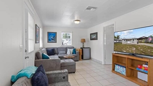 A living room with a grey sofa, a television, and a small table. There are windows and a door in the room. - Fenway Fiddler - Steinhatchee (Steinhatchee)