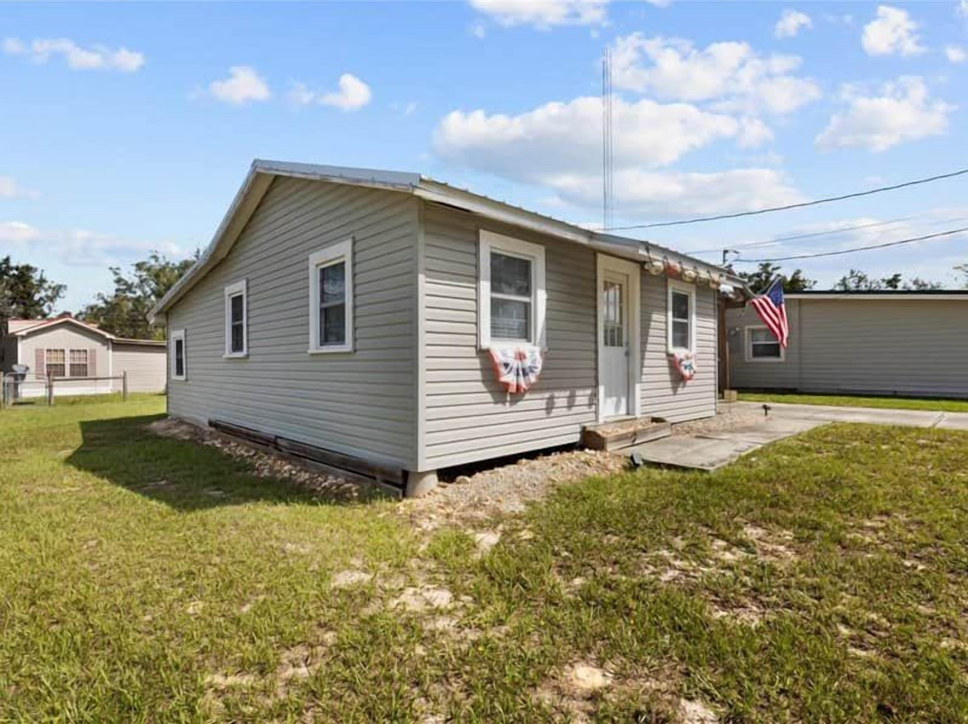 A single-story mobile home with a gabled roof, a front porch, and a small front yard.