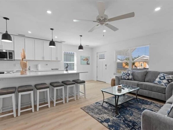 A modern kitchen with white cabinets, a central island with stools, and a ceiling fan. - The Pelican Pad - Steinhatchee (Steinhatchee)