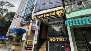 Un hotel con un llamativo letrero que dice 'MBee Hotel', una entrada visible con una escalera y una puerta principal con reja.