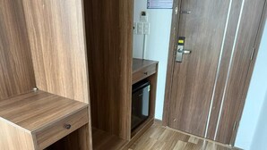 Un armario de madera con un pequeño estante y un cajón, un escritorio de madera con una silla, y una puerta con cerradura.