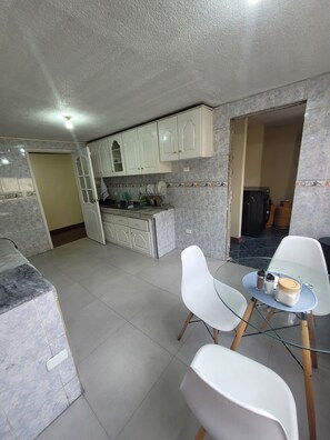 A compact kitchen with white cabinets, a dining area with a glass table, and a tiled floor. - Spacious apartment in downtown Quito, perfect for your getaway (Quito)