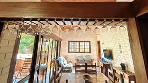 A dining area with wooden tables and chairs, a brick wall, and a view of the outdoors. - House in the wonderful Pauba Condominium, a small village. (São Sebastião)
