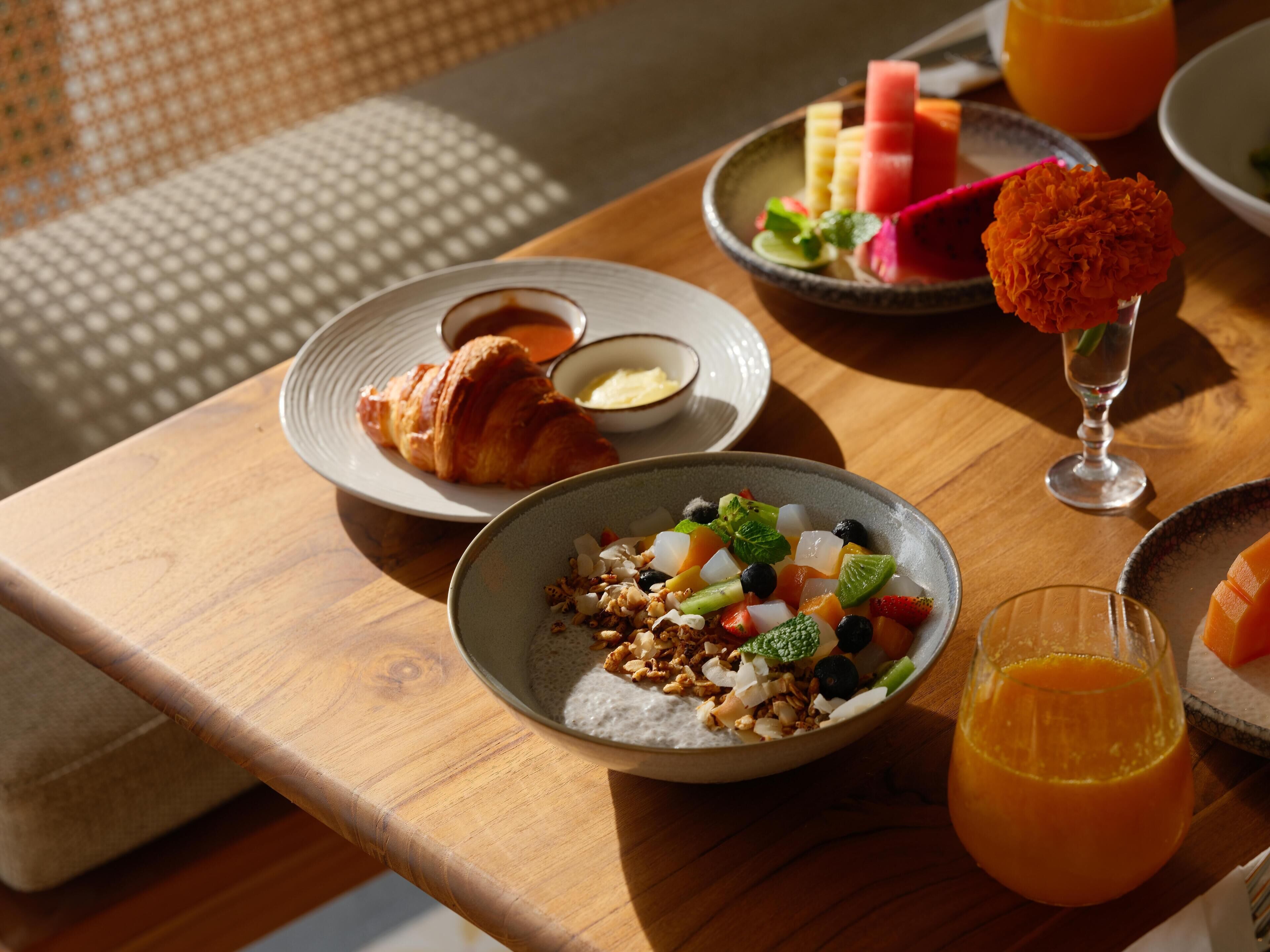 Ein Frühstückstisch mit Croissants, Obstsalat und einem Glas Orangensaft.