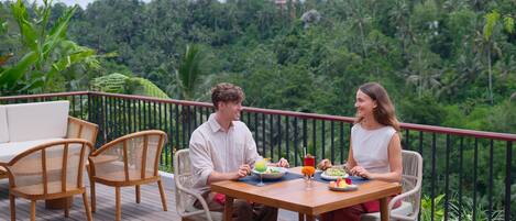 Una pareja cena en una terraza de madera con vistas a un paisaje verde exuberante.