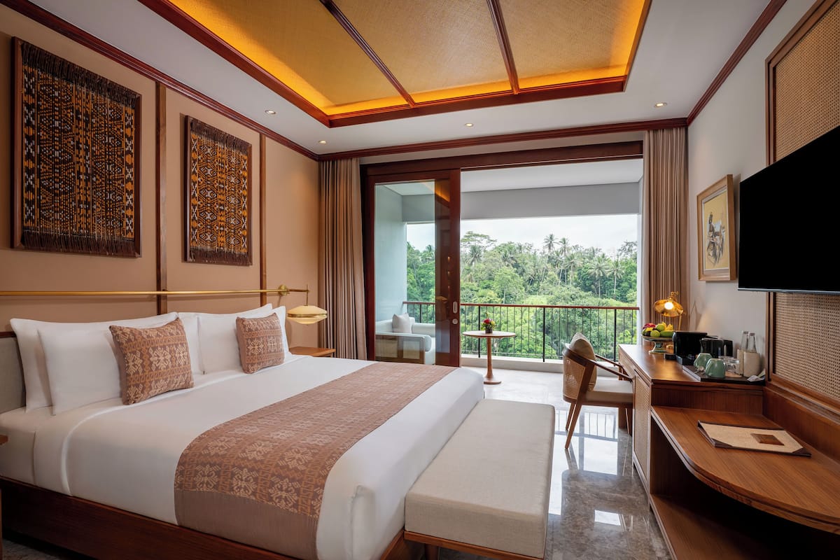 A hotel room with a large bed, a desk with a chair, a television, and a balcony with a view of the outdoors.