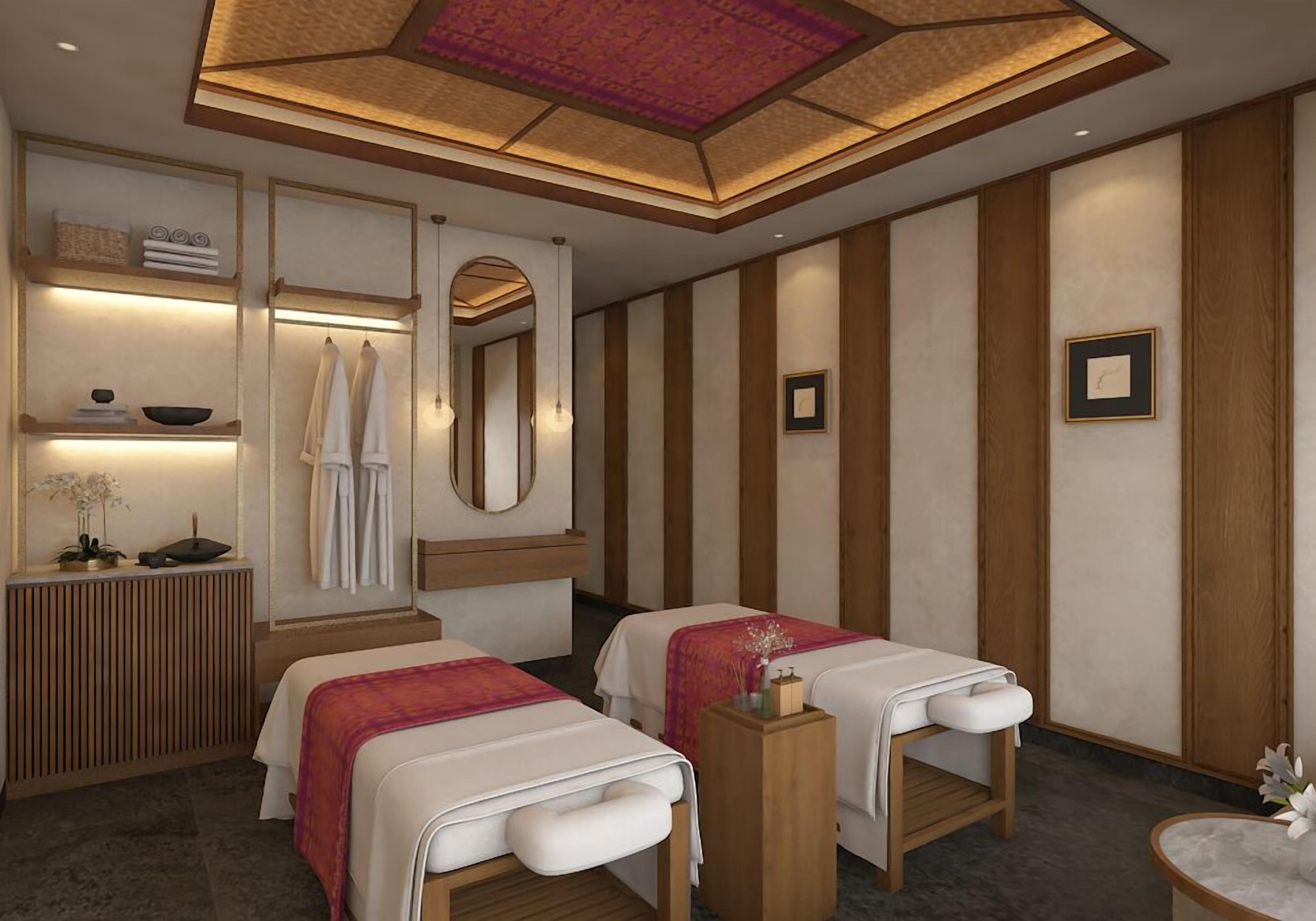 A spa room with two beds, a wooden console, a mirror, and a ceiling with a geometric pattern.