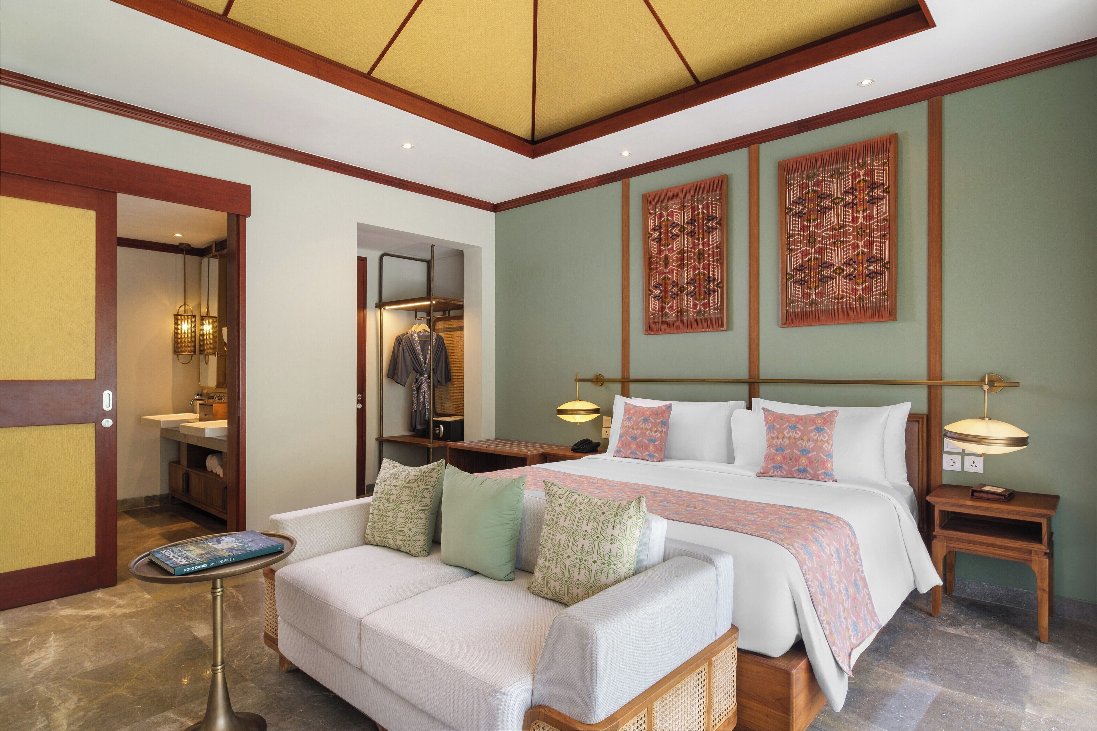 Quarto de hotel com uma cama, um sofá, uma mesinha de cabeceira, um abajur e um espelho.