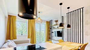 Une cuisine moderne dotée d’une cuisinière intégrée, d’un coin repas avec des chaises jaunes et d’une grande fenêtre avec des rideaux.