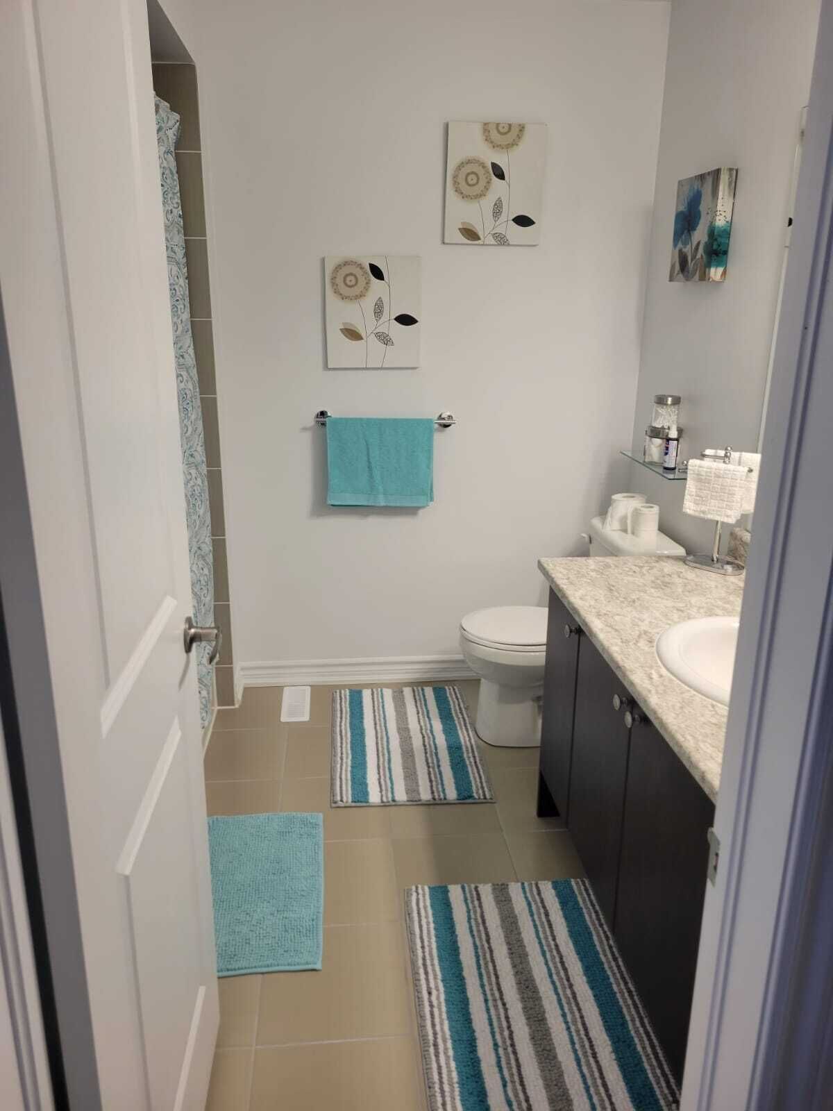 A bathroom with a toilet, sink, and two towels on towel racks. There are two rugs on the floor.