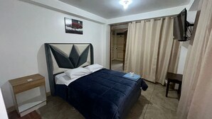 Una camera da letto con un letto, un comodino, una TV a parete e una porta che dà su un'altra stanza.