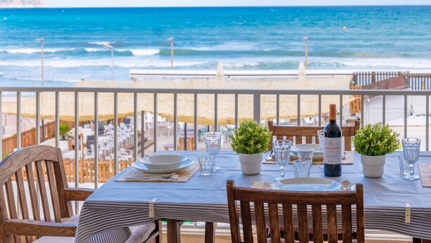 A table set for two with a view of the ocean, potted plants, and a bottle of wine. - TUGORES SIMÓ 2º A - Charming apartment on the beachfront in Can Picafort – Free Wi-Fi (Muro)
