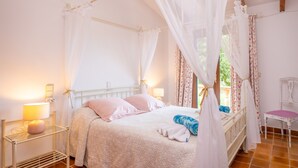 Ein Schlafzimmer mit einem Himmelbett, einem Nachttisch mit Lampe und einem Sessel.