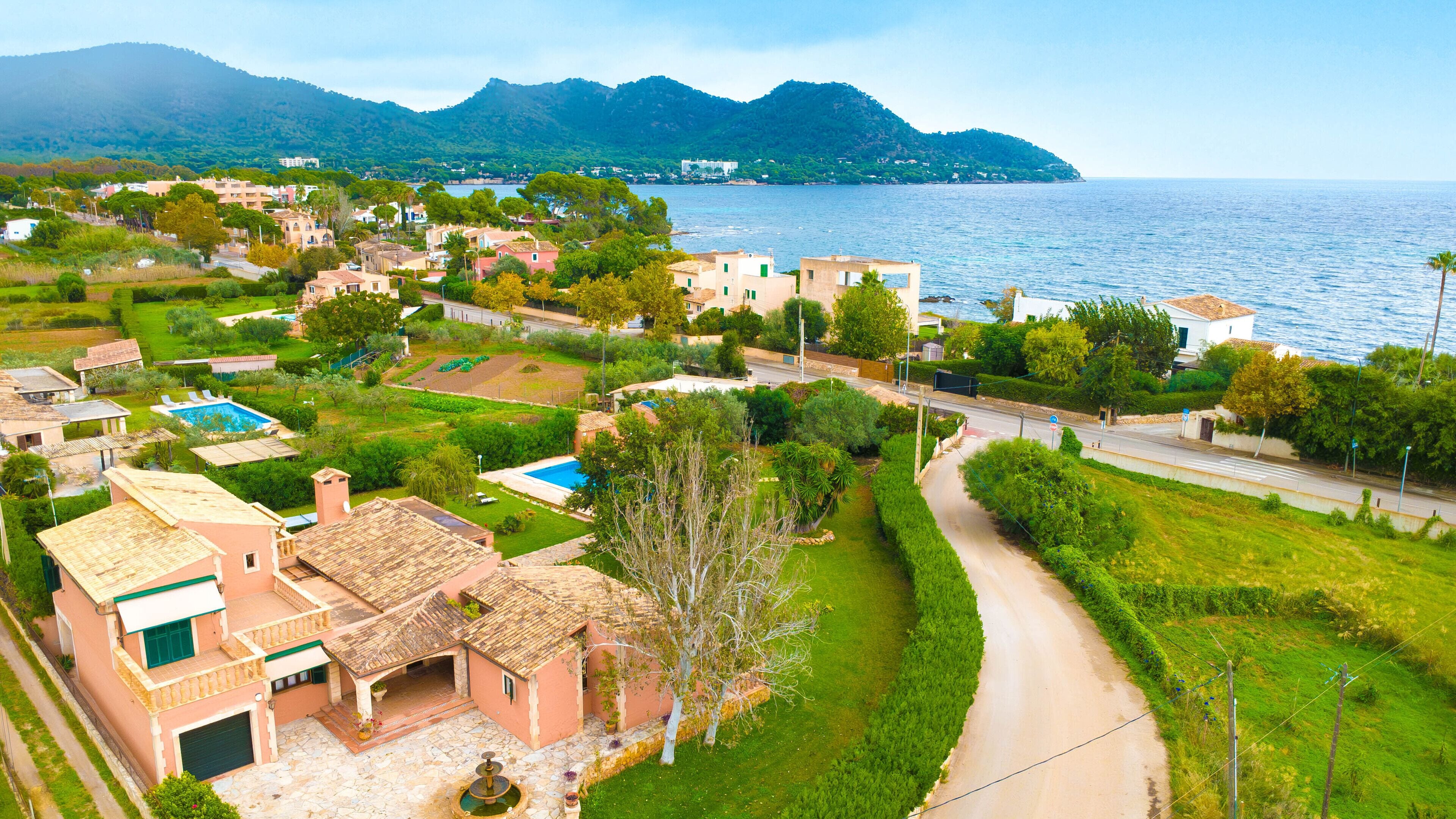 A coastal residential area with houses, a swimming pool, and a road leading to the sea.