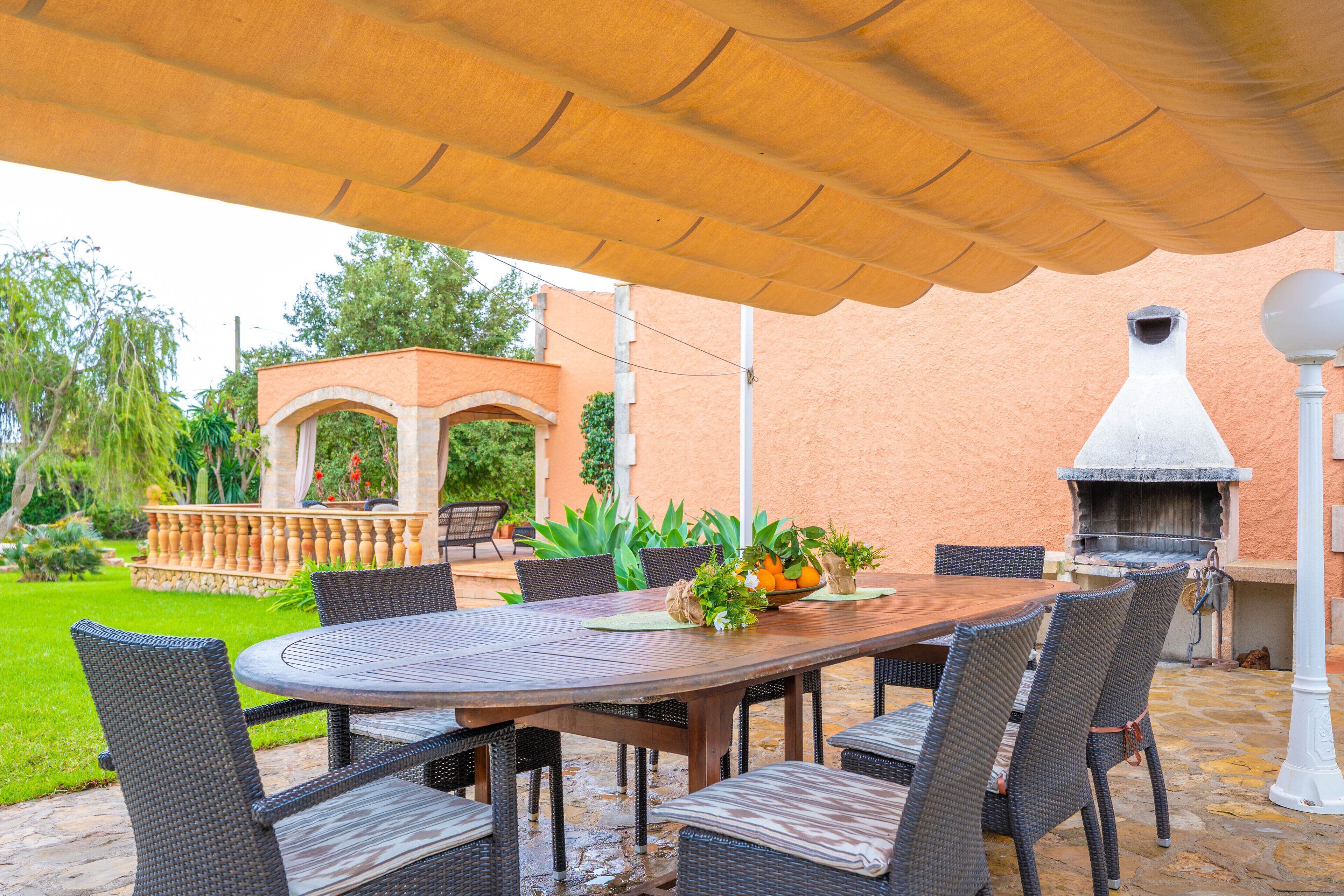 An outdoor patio with a round table, wicker chairs, a grill, and a pergola.