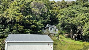 A rustic wooden building with a metal roof, surrounded by lush greenery and a small house in the background. - Entire home in Auckland, New Zealand (Auckland)