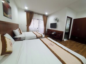 A hotel room with two beds, a desk with chairs, a TV, and a wardrobe. - GOLD KIM PHÚ - Hotel Da Lat (Cam Ly - Da Lat)