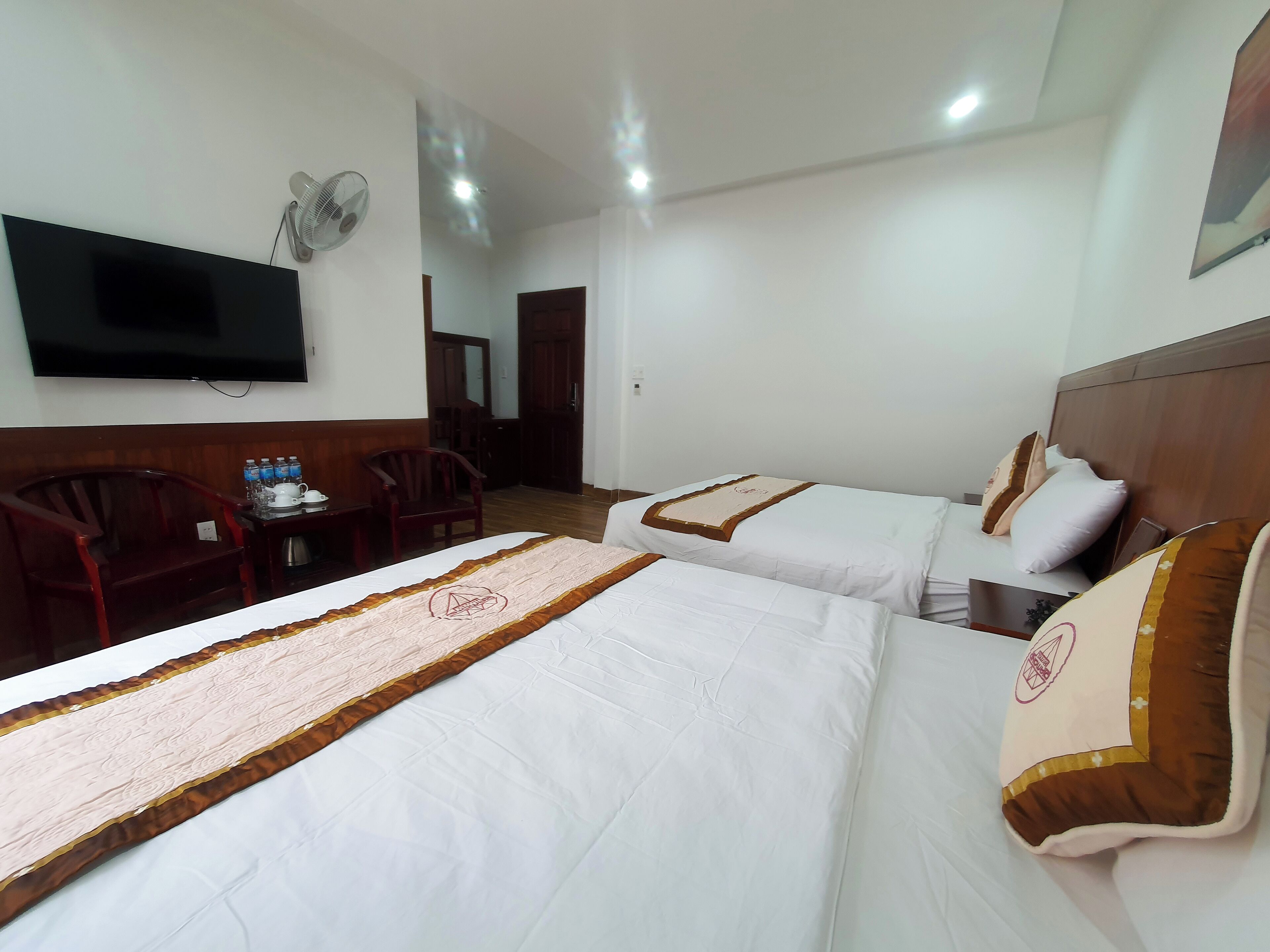 A hotel room with two beds, a TV, a desk with a chair, and a small table with bottles.