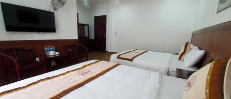 A hotel room with two beds, a TV, a desk with a chair, and a small table with bottles.