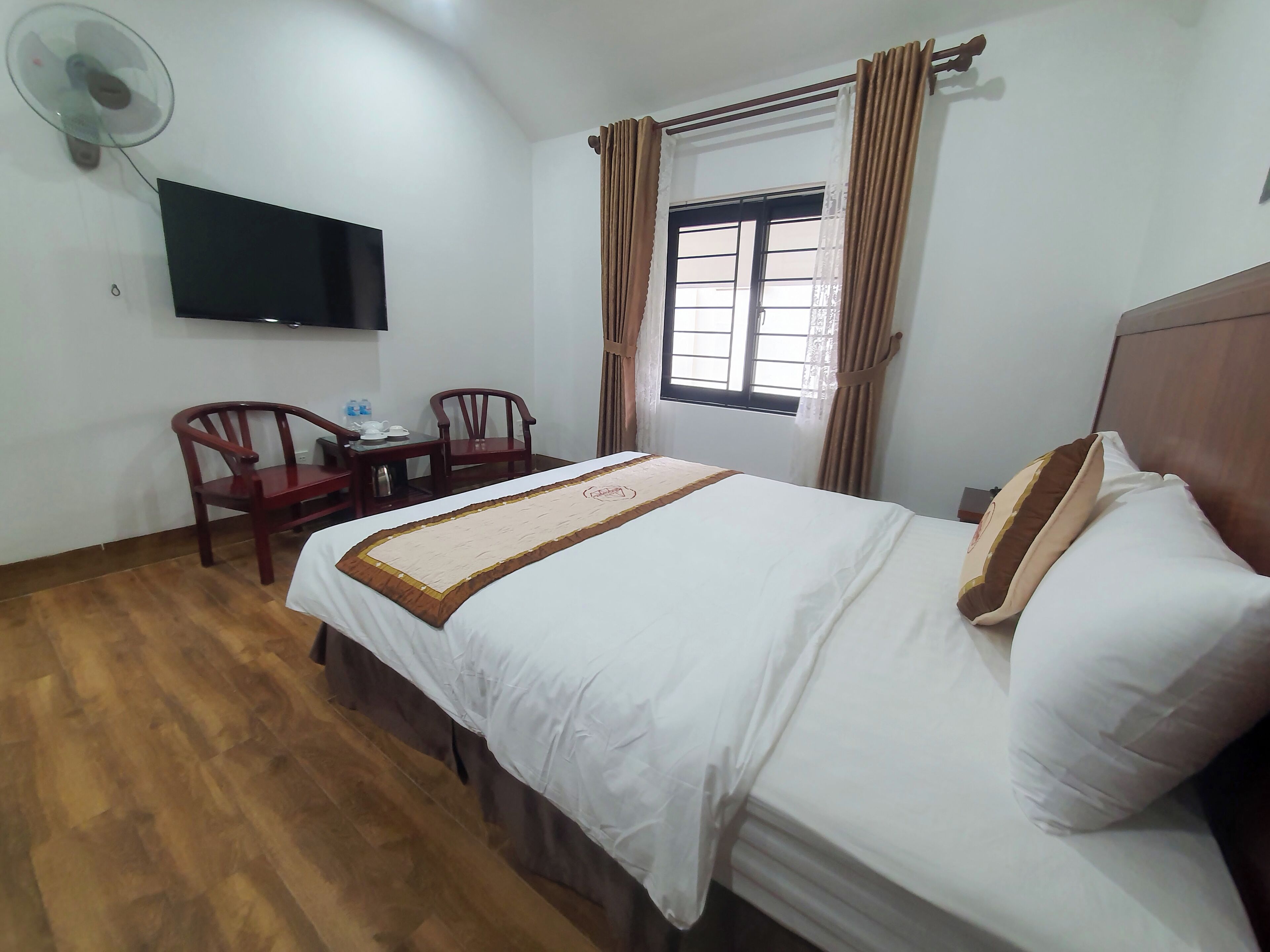 Een hotelkamer met een bed, een bureau met stoelen, een flatscreen televisie aan de muur en een raam met gordijnen.