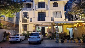 A hotel with a prominent sign, two parked cars, and potted plants in front. - GOLD KIM PHÚ - Hotel Da Lat (Cam Ly - Da Lat)