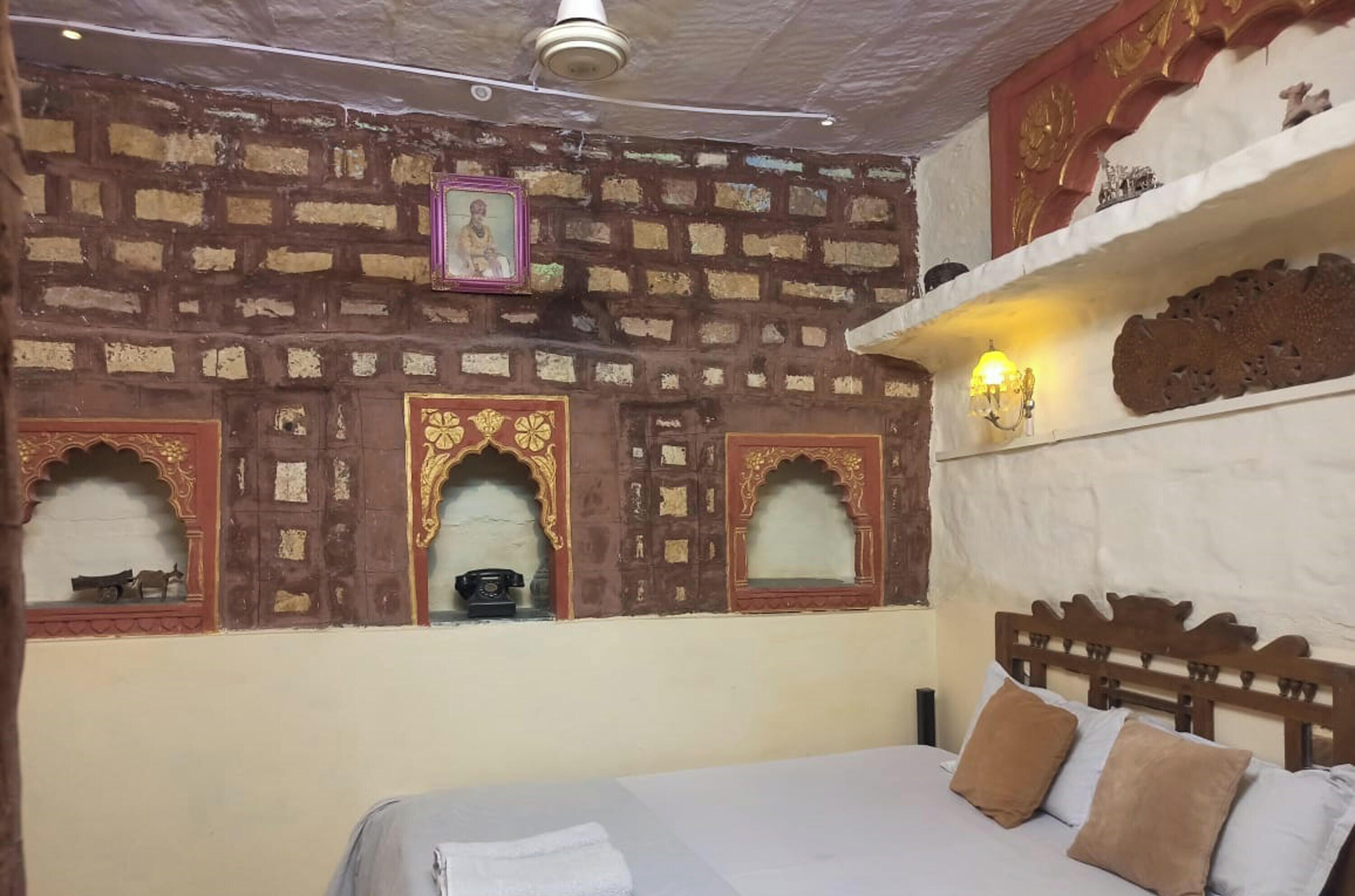 A room with a bed, a wall with decorative arches, a shelf with items, and a ceiling light.