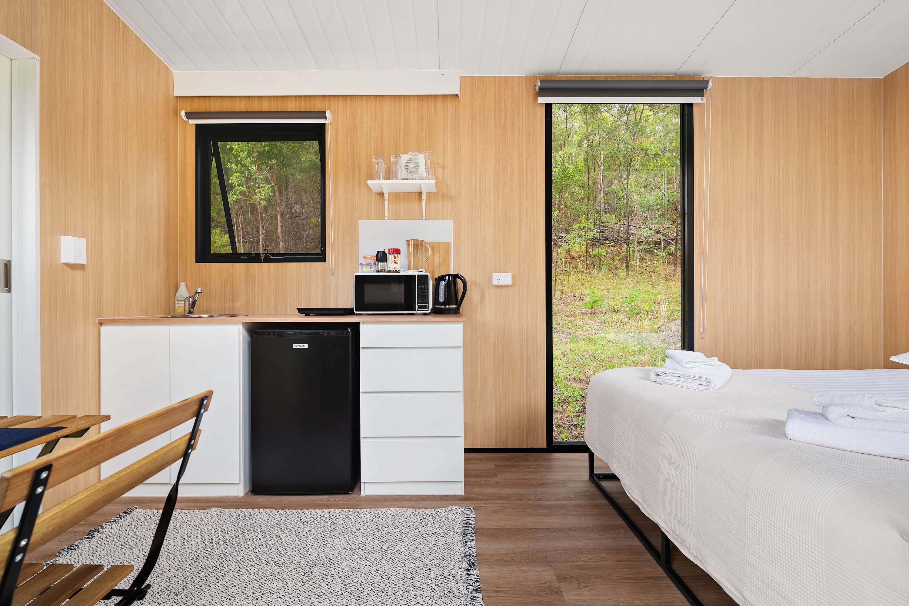 Ein modernes Schlafzimmer mit einem großen Bett, einem eingebauten Schreibtisch, einer Mikrowelle und Blick ins Freie.