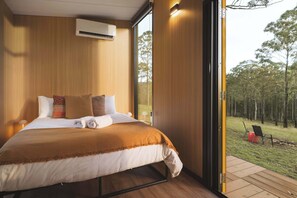 Un dormitorio moderno con una cama grande, un equipo de aire acondicionado empotrado y vistas a una zona boscosa a través de un ventanal.