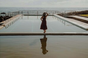 Une personne se tient au bord d’une piscine, avec vue sur l’océan.