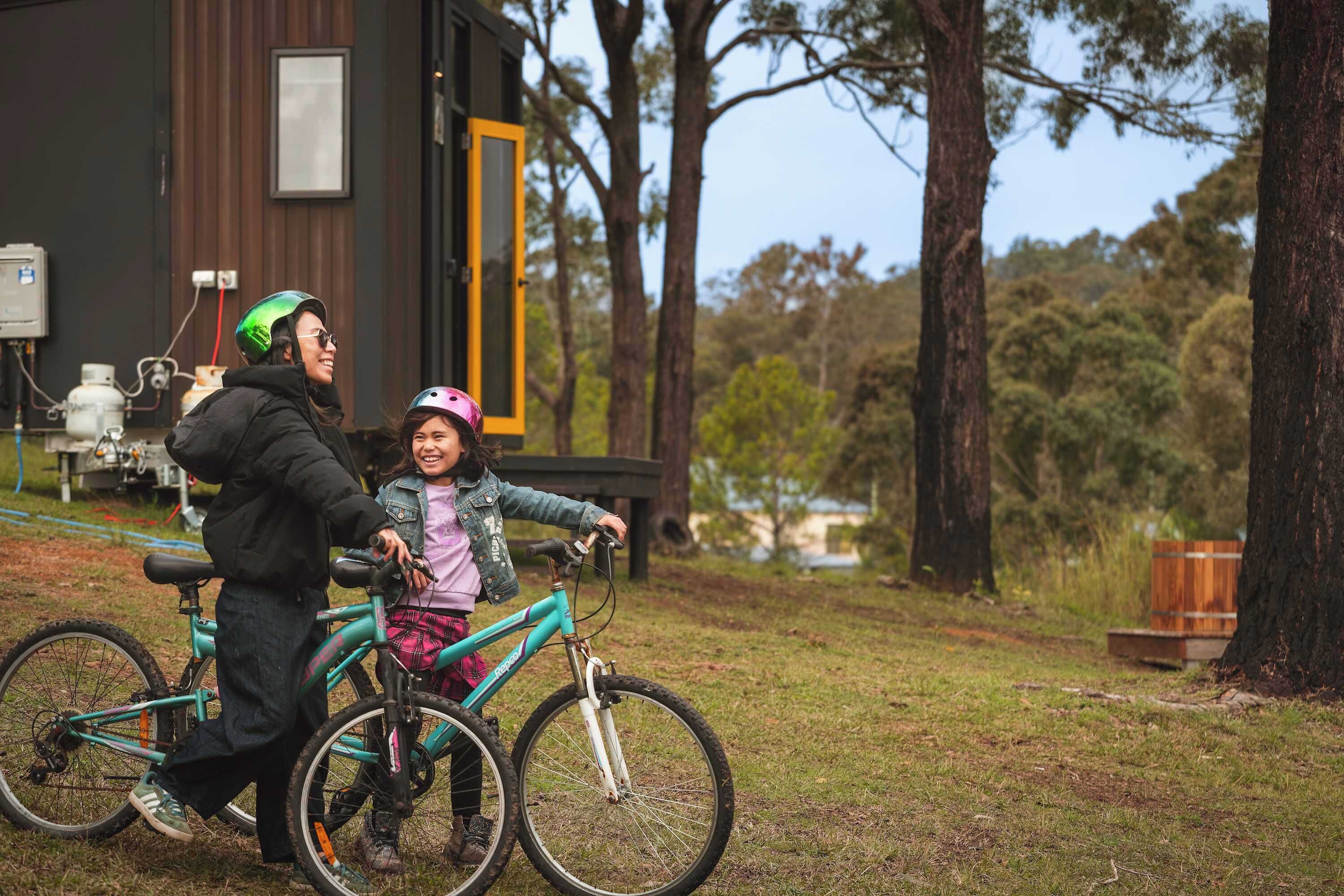 Une personne à vélo avec un enfant, un bâtiment avec une porte et des arbres en arrière-plan.