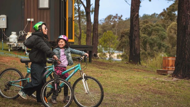 Une personne à vélo avec un enfant, un bâtiment avec une porte et des arbres en arrière-plan.