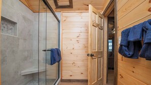A wooden interior with a glass shower enclosure, wooden walls, and a blue towel hanging on the right.