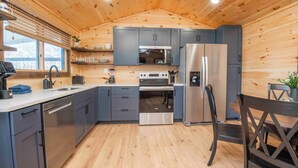 A modern kitchen with wooden walls, grey cabinets, stainless steel appliances, and a wooden dining table with chairs.
