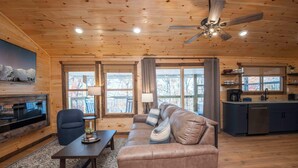 A cozy cabin interior with a wooden ceiling, a sofa, a dining table, and a kitchen area.