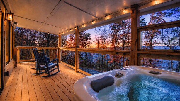 A wooden deck with a hot tub and a rocking chair, overlooking a scenic autumn view.