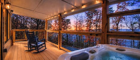 A wooden deck with a hot tub and a rocking chair, overlooking a scenic autumn view.