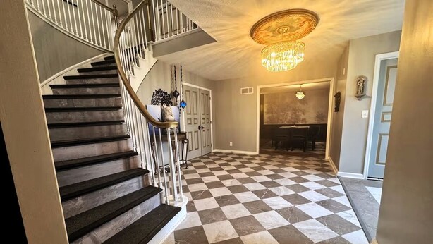Una escalera con piso a cuadros que conduce a un comedor con candelabro.