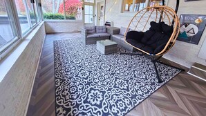 Una habitación acogedora con un ventanal grande, un sillón colgante, un sofá y una alfombra estampada.