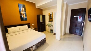A hotel room with a large bed, a wardrobe, a bathroom with a glass sink, and a door leading to another room. - Hommy Inn Timoho (Yogyakarta)