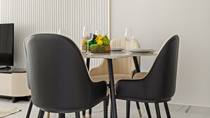 Ruokailutilassa on pyöreä pöytä, kaksi mustaa tuolia, beige sohva ja hedelmäkori.