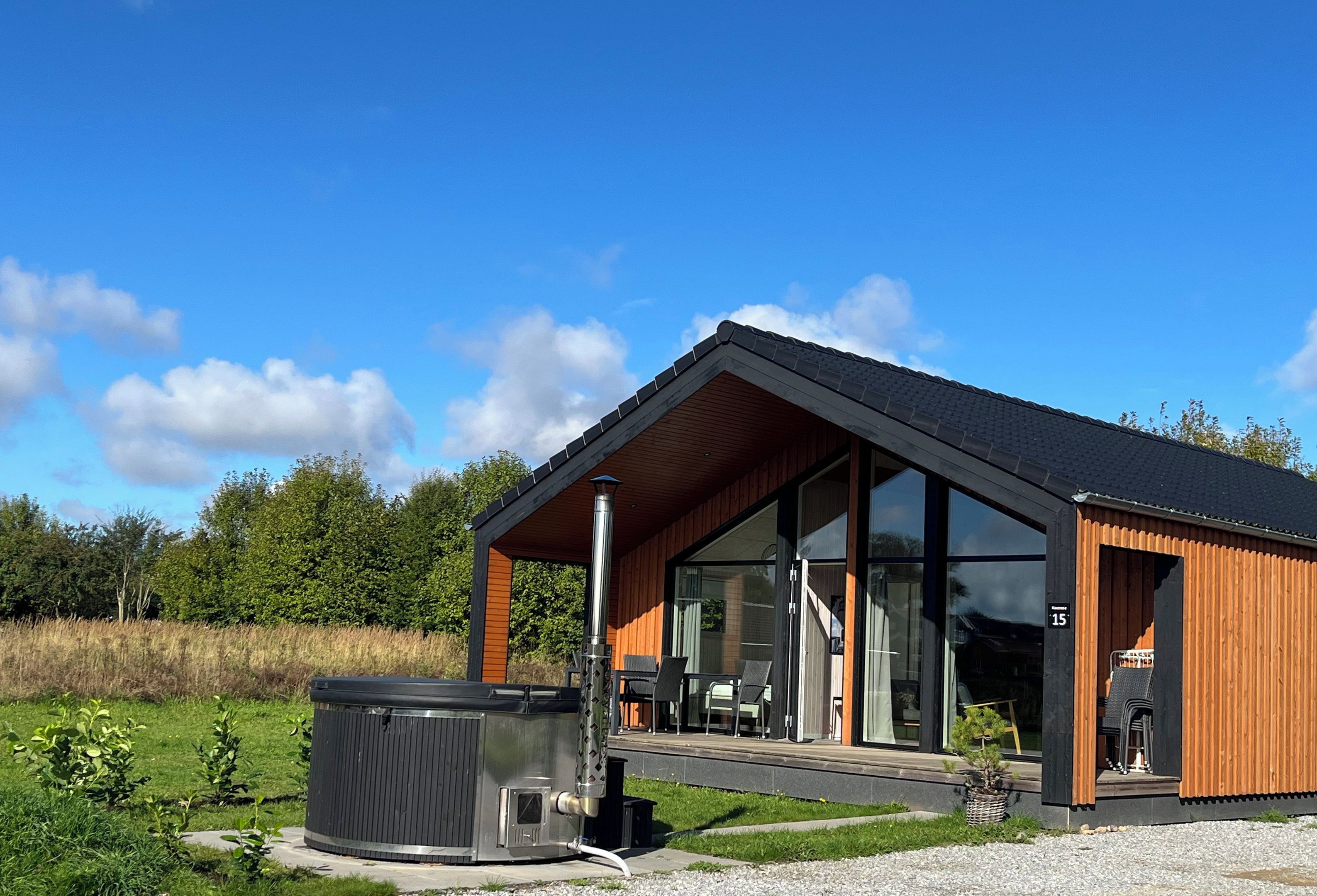 Ett modernt hus med en stor glasdörr, ett bubbelbad och en träfasad.